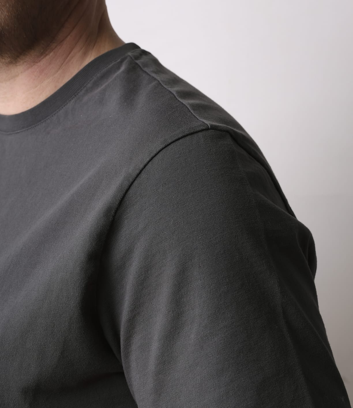 Close-up of a person wearing the Best Made Co Standard T-Shirt in Faded Black, showing the upper chest, shoulder, and part of the neck against a plain light background. The person's face is partially out of frame.