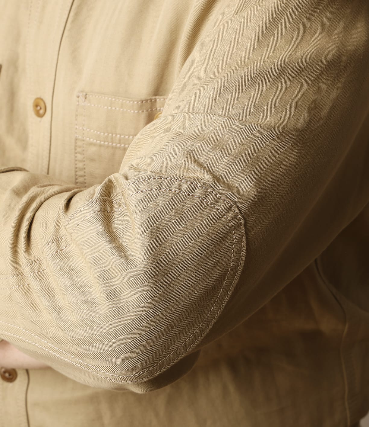 A close-up of a person's arm wearing the Best Made Co. Cotton-Linen Workshirt Tan, featuring an elbow patch and pocket seam detail, made in Portugal.