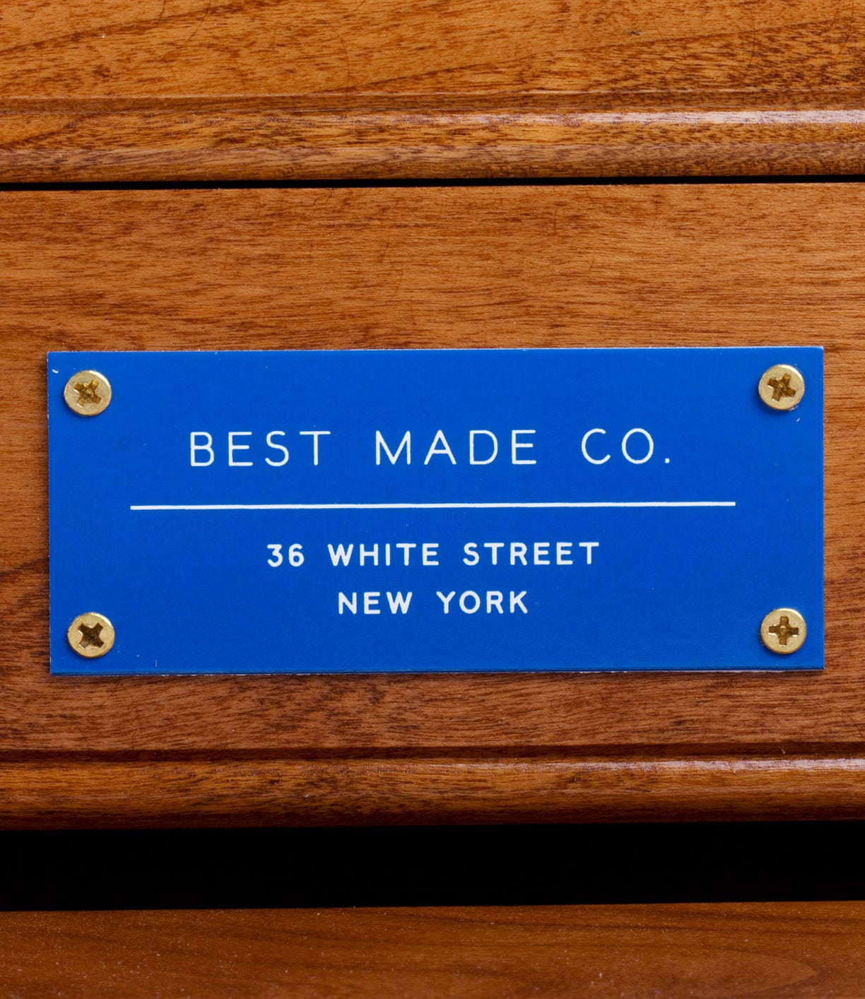 A blue plaque with gold screws on wood—possibly from a Best Made Co. 41D Gerstner Chest 2026—reads: BEST MADE CO. 36 WHITE STREET NEW YORK.
