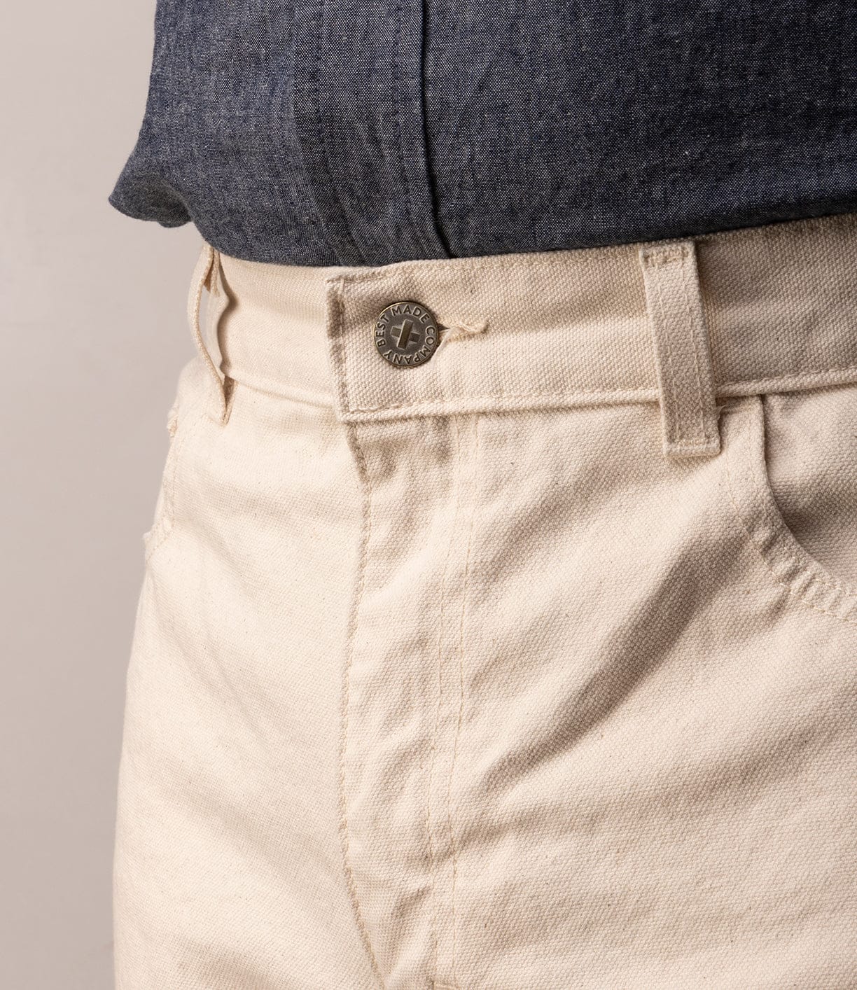 Close-up of a person wearing Best Made Co's Standard 5-Pocket Pant M2 Undyed, heavyweight cotton, classic straight leg with metal button and belt loop, styled with a tucked-in blue textured shirt.