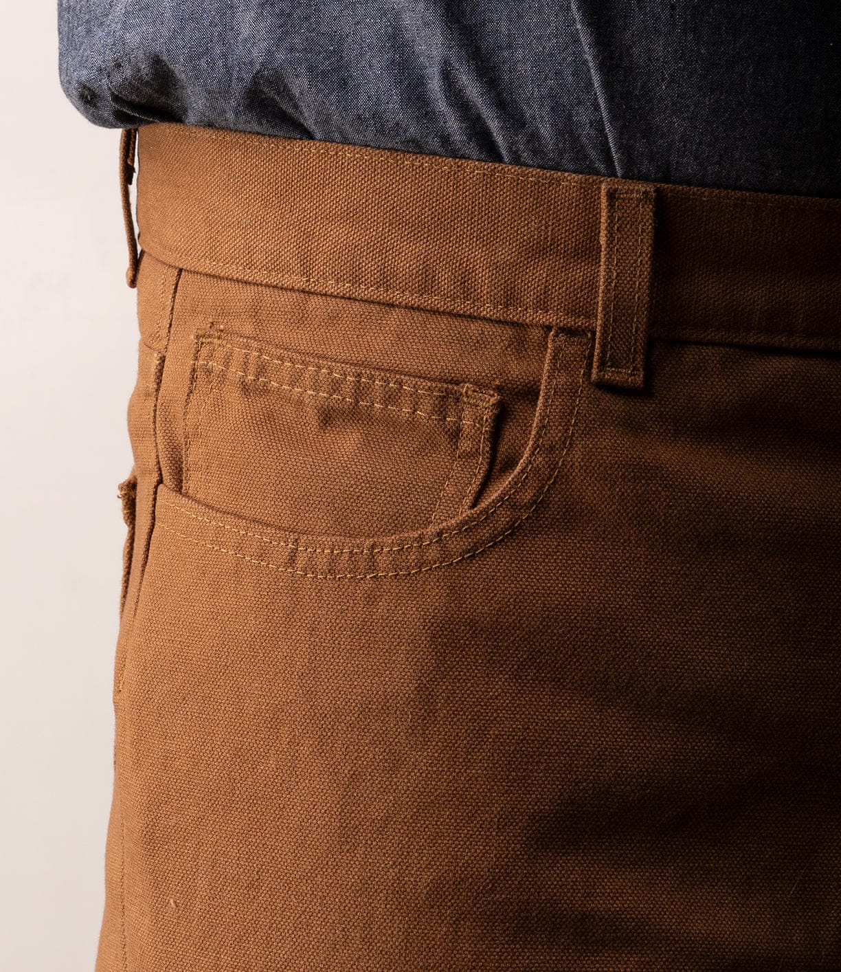Close-up of a person in Best Made Co’s Standard 5-Pocket Pant M2 Field Brown, featuring visible stitching, heavyweight cotton texture, and belt loops. Pants are paired with a tucked-in dark blue shirt.