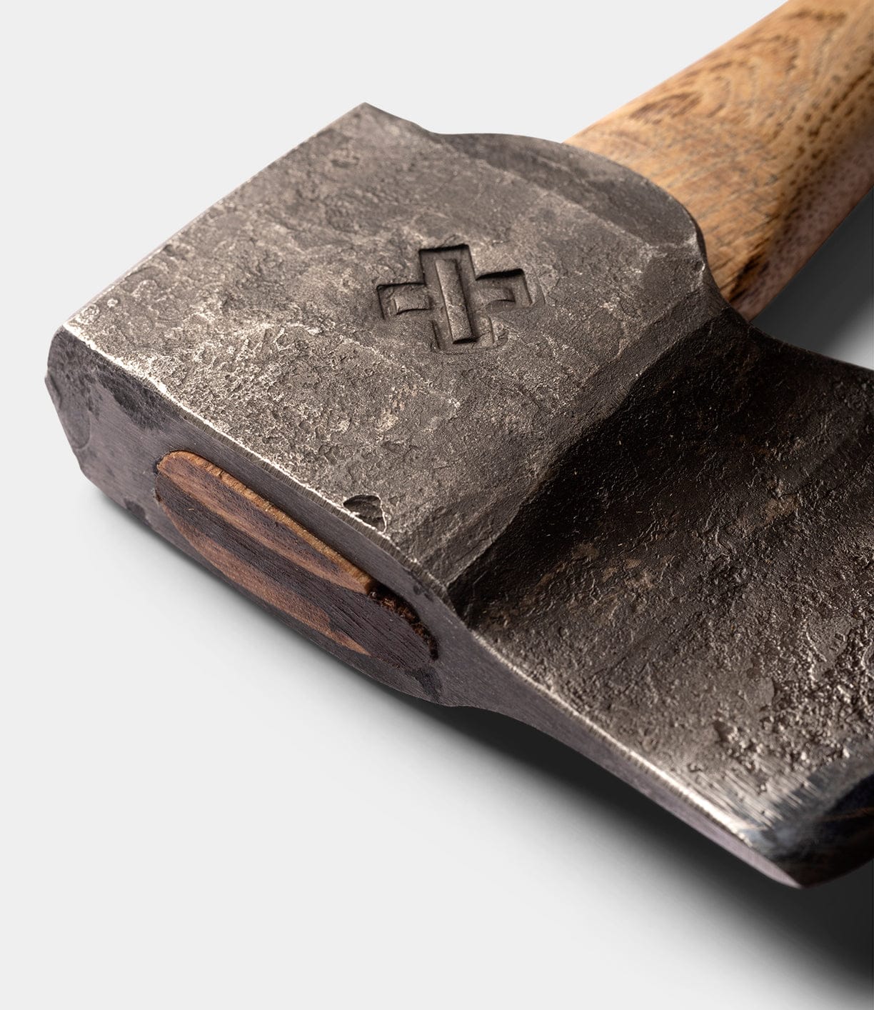 Close-up of the Spark (Straight-Hold Edition) axe head by Best Made Co., featuring a cross imprint on high-carbon steel. The Appalachian hickory handle is smooth and polished. Set against a plain, light-colored background.