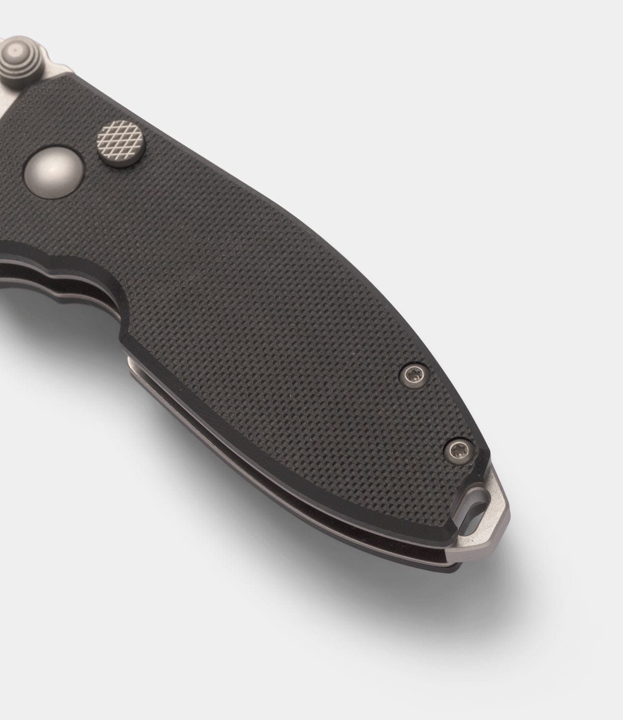 Close-up of the Best Made Co CRKT Squid knife's black textured handle, showing visible screws, a lanyard hole, and a button lock mechanism against a plain white background.