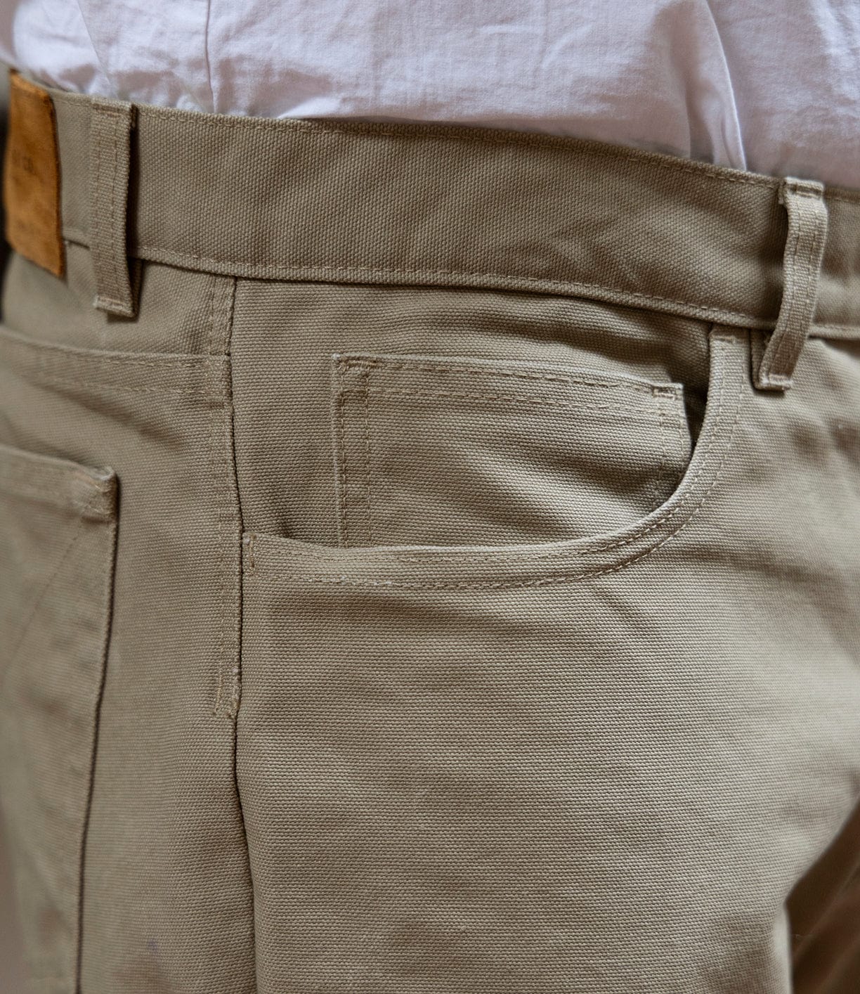 Close-up of Best Made Co Canvas 5-Pocket Pant Mark 2 - Undyed in beige, featuring classic straight leg fit, front and coin pockets, belt loops, and visible fabric texture with stitching details, styled with a tucked-in white shirt.