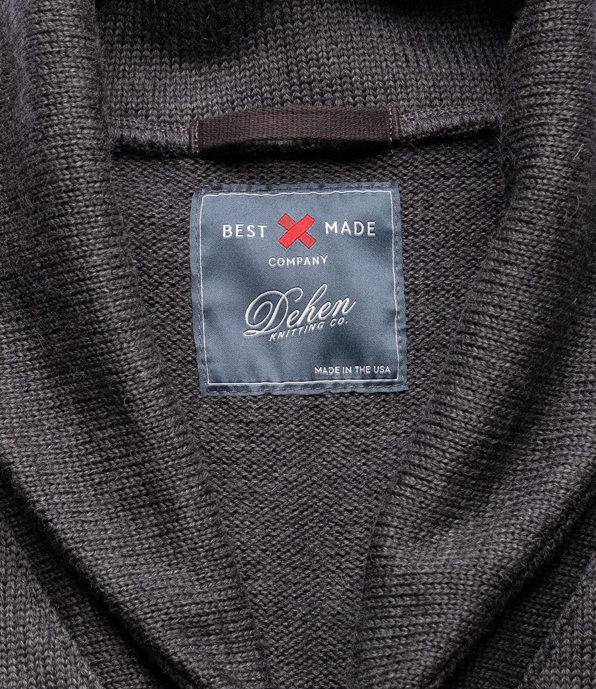 Close-up of the Dehen Shawl Neck Sweater in Charcoal by Best Made Co., featuring a blue tag stitched inside the collar—a timeless piece of American workwear.