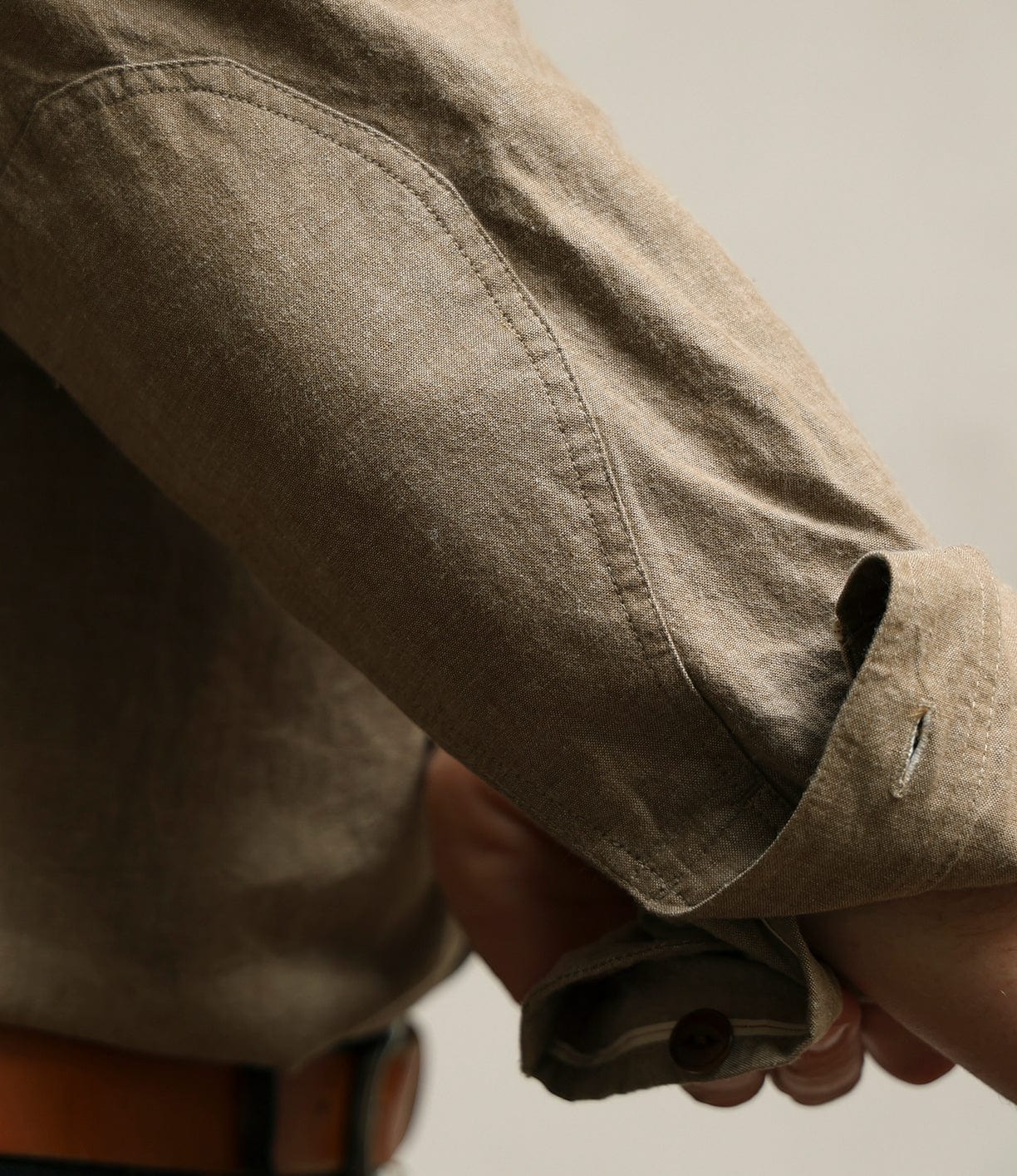 A close-up of a person's arm in the Best Made Co. Cotton/Linen Herringbone Workshirt in tan, with the cuff unbuttoned and slightly rolled, revealing a buttonhole and part of a dark brown belt at the waist.