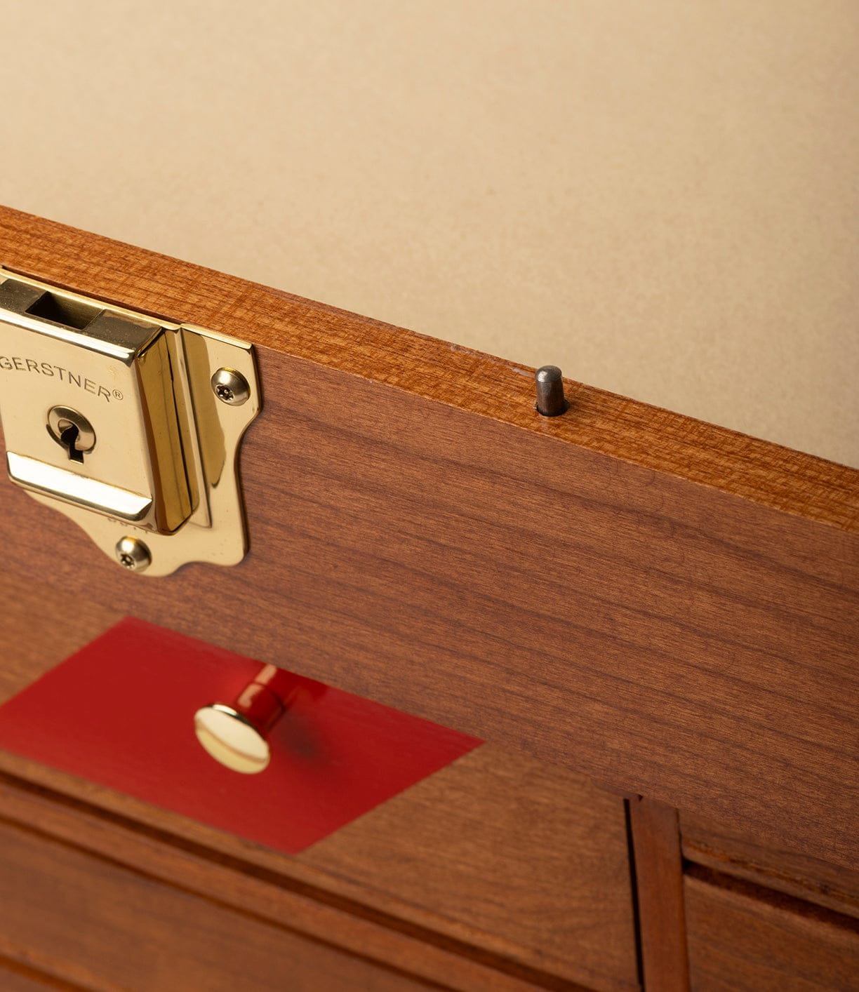 Close-up of the Gerstner 41D Founder’s Edition by Best Made Co., a wooden chest with a brass lock, metal peg, and red panel with gold knob. Its light brown finish recalls an American cherry tool chest. Set against a plain beige background.