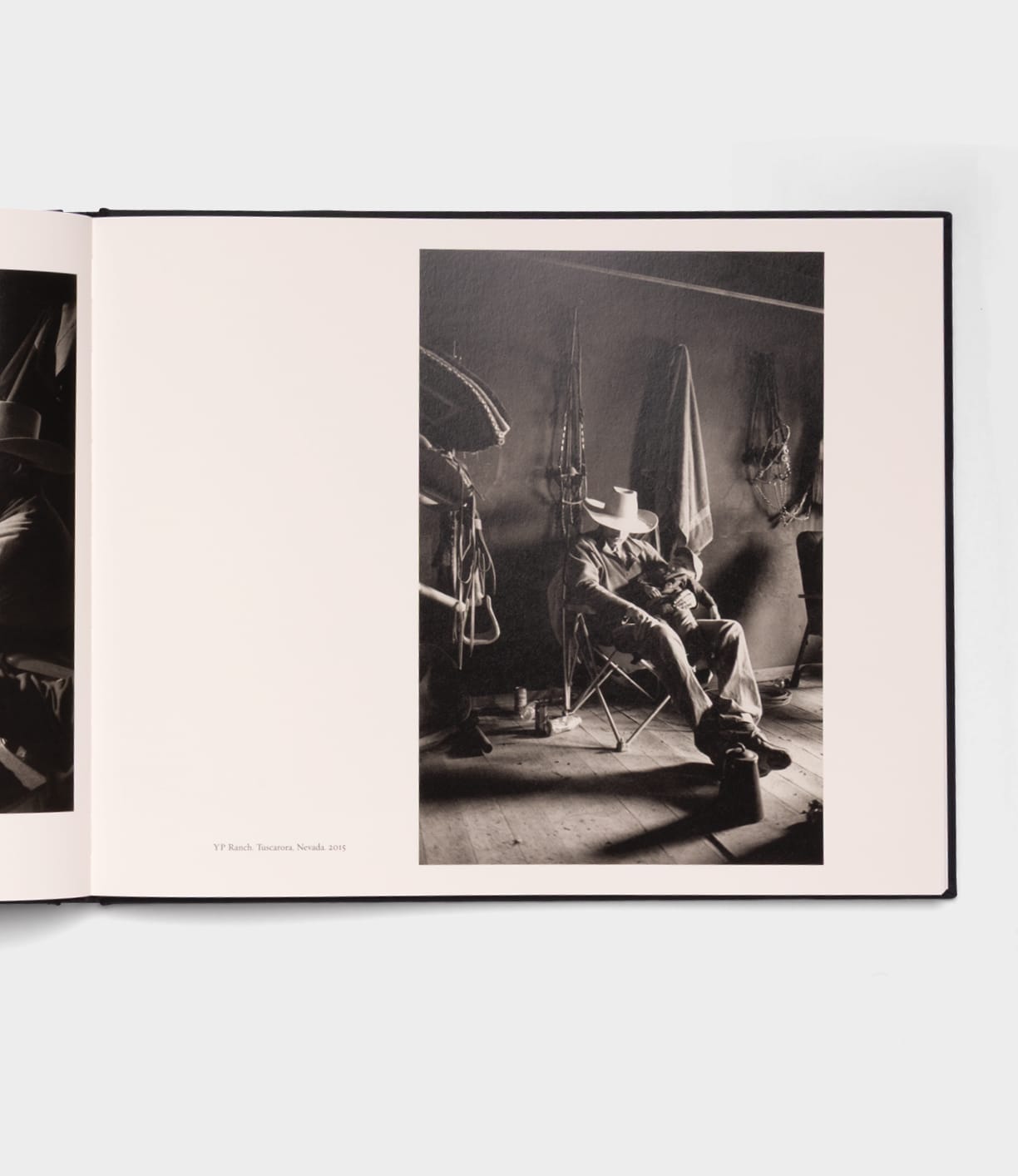 A black-and-white photo in Best Made Co.'s photography book "Open Range" depicts a person in a cowboy hat on a folding chair, surrounded by saddles and ranch equipment in dim light, evoking the quiet storytelling of Robert Adams.