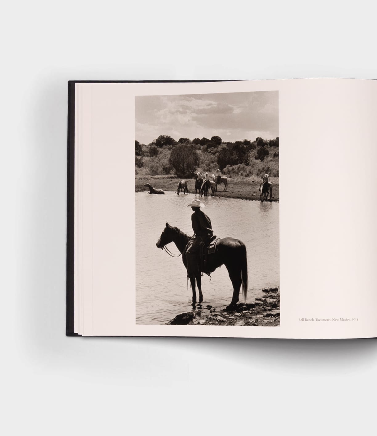 An open photography book, "Open Range" by Best Made Co., shows a black-and-white image of a rider on horseback near water, with other horses and riders in the background among sparse trees—evoking classic landscapes.