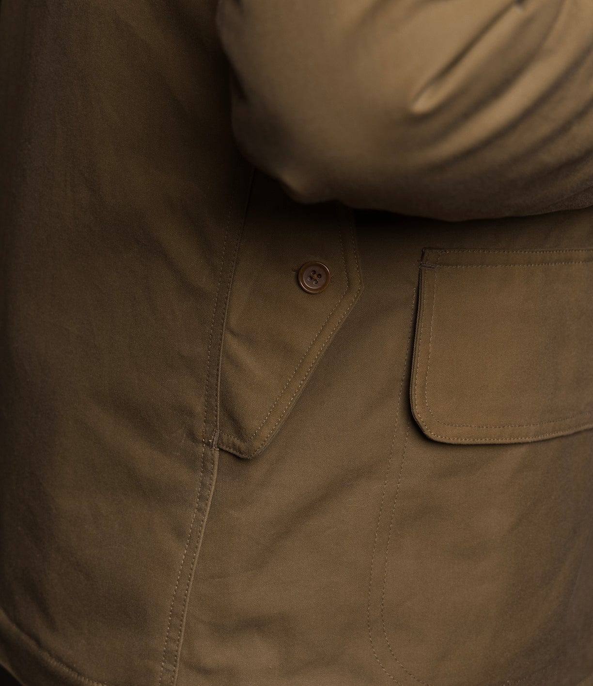 Close-up of the Best Made Co. Wool-Lined Waxed Field Jacket in tan, featuring a buttoned flap pocket and detailed stitching that highlight the textured waxed cotton. Part of an arm is visible in the upper right corner.