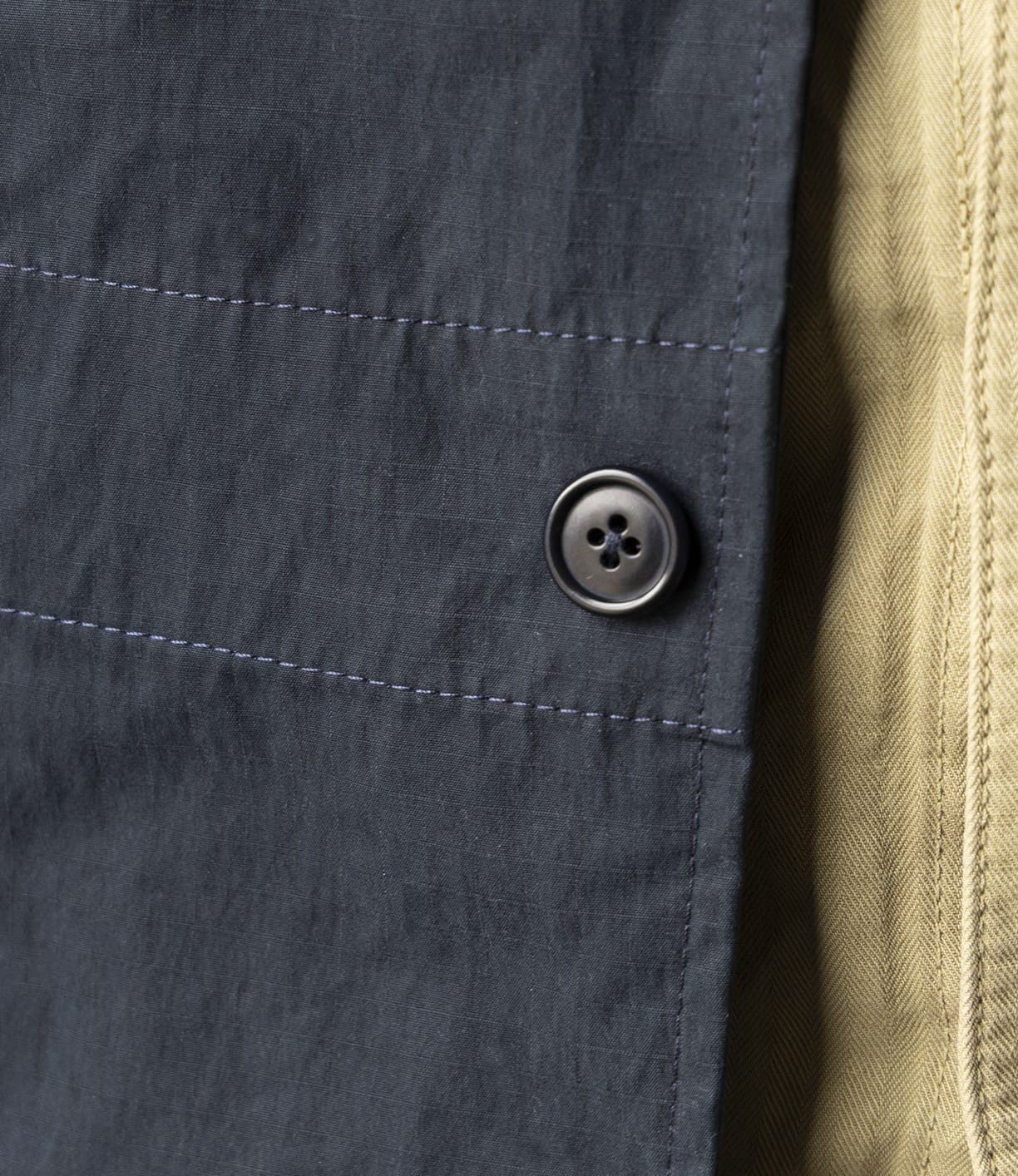 Close-up of blue-gray fabric with a black button, next to yellow-beige textured fabric—highlighting Best Made Co’s craftsmanship and attention to detail in the Possibilities Jacket Navy.