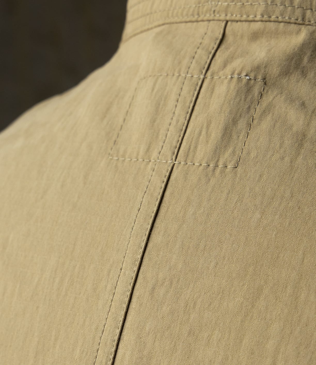 Close-up of the back of the Possibilities Jacket Tan by Best Made Co, featuring visible stitching, a rectangular patch near the neckline, and lightweight textured fabric that highlights its American artisanal craftsmanship.