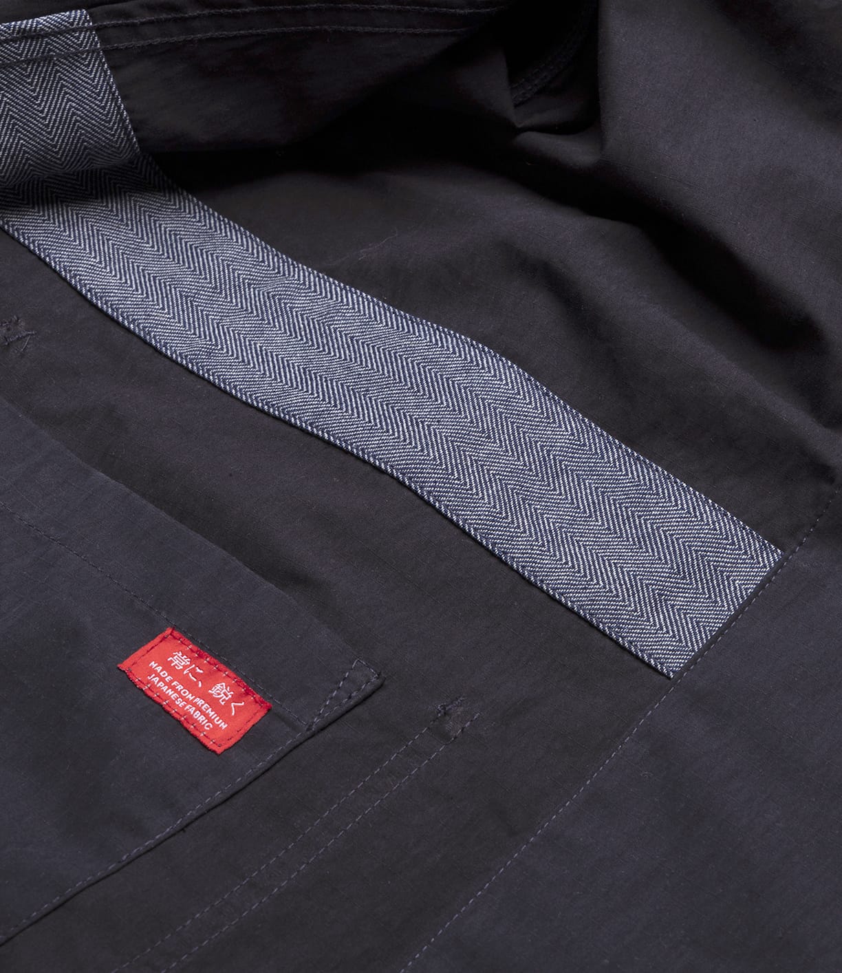 Close-up of the Possibilities Jacket Navy by Best Made Co, showing its durable, lightweight build, Japanese herringbone-patterned lining, and a red fabric label with white text sewn above a pocket.