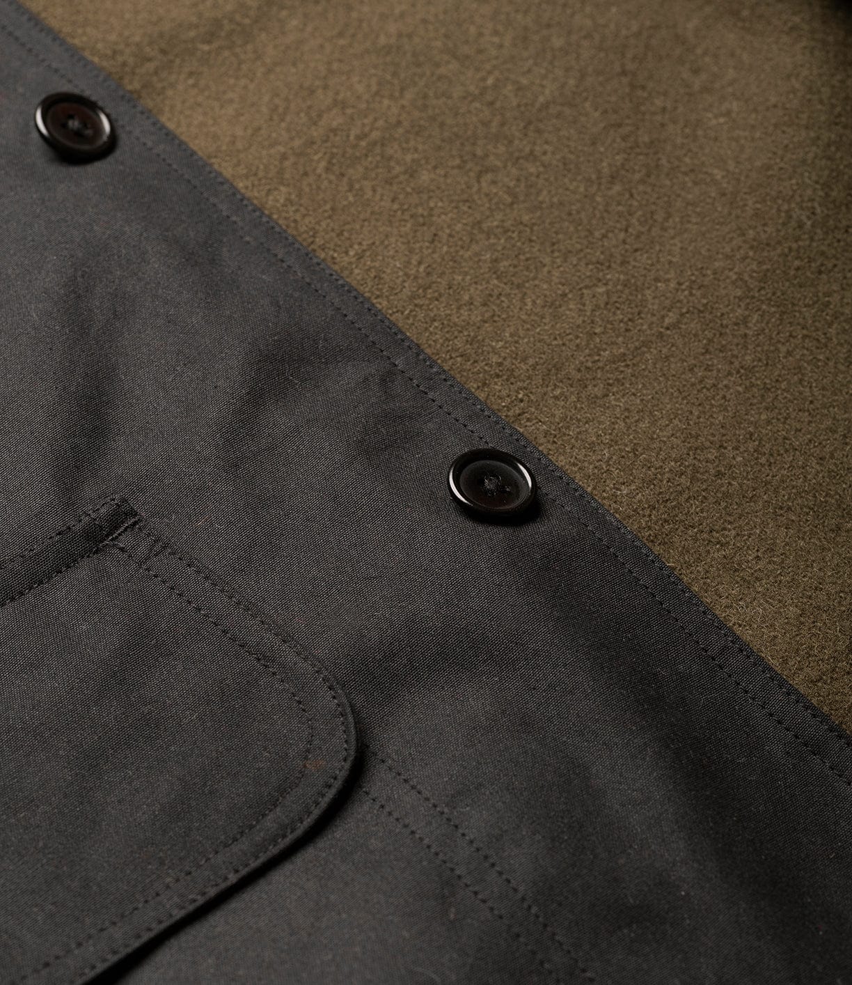Close-up of Best Made Co.'s Wool-Lined Waxed Field Jacket Black, featuring dark buttons, olive green wool lining, and a black canvas pocket with visible stitching—a functional yet stylish outerwear piece.