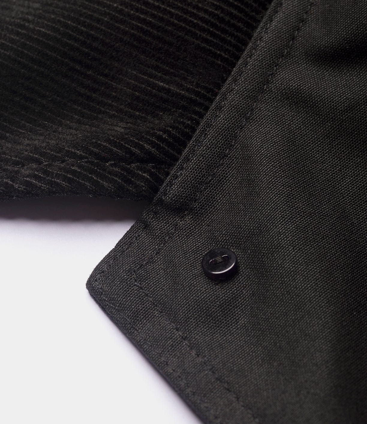 Close-up of a black fabric collar with a black button, featuring fine stitching and texture, from the Best Made Co. Wool-Lined Waxed Field Jacket Black, set against a plain white background.