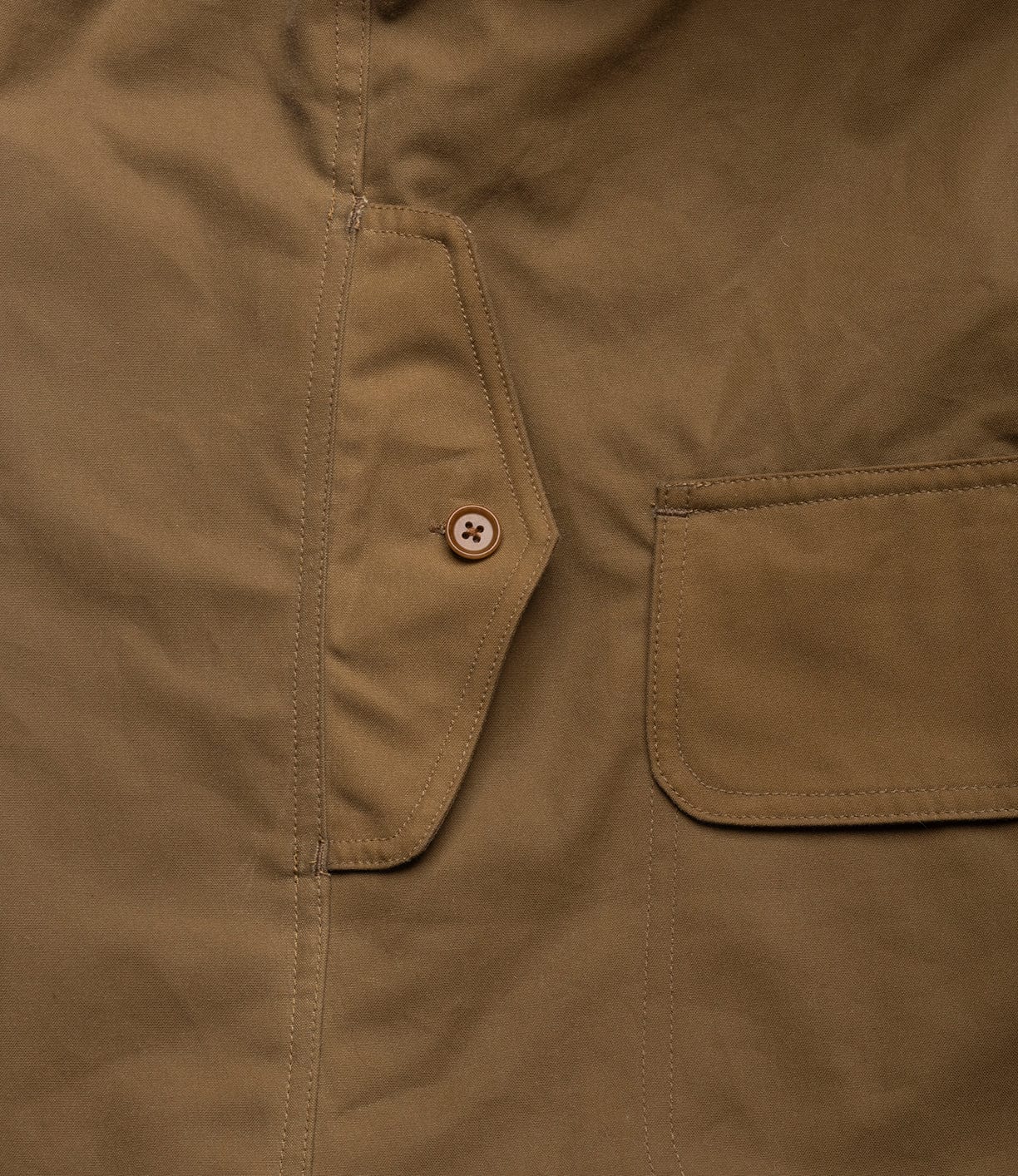 Close-up of the Best Made Co. Wool-Lined Waxed Field Jacket Tan, highlighting two pockets—a button-flap pocket and a rectangular flap pocket—crafted from sturdy, weather-resistant, textured waxed cotton.