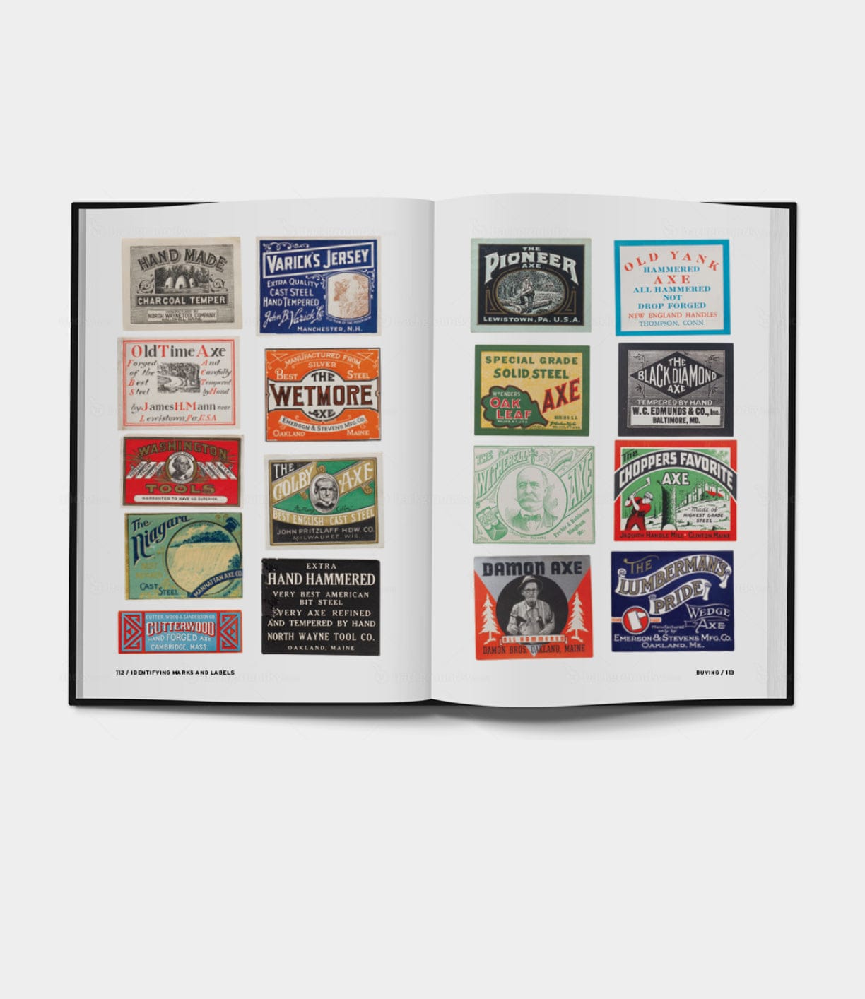 An open book displays vibrant vintage axe label designs on each page, echoing the style of Buchanan-Smith’s Axe Handbook by Best Made Co. The labels feature distinct graphics, text, and ornate borders set against a clean white background.