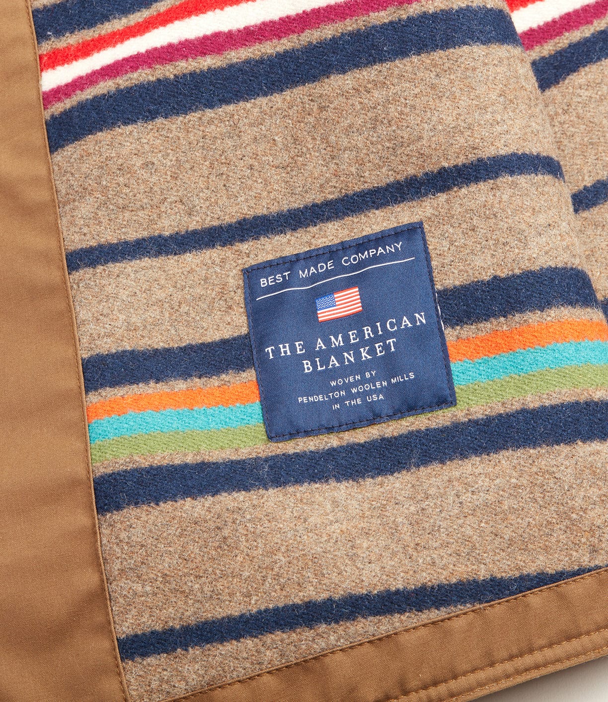 A close-up of the Best Made Co. Wool-lined Waxed Field Jacket in tan shows its colorful wool lining and blue label, woven in the USA, evoking classic comfort. A small American flag adds a patriotic touch.
