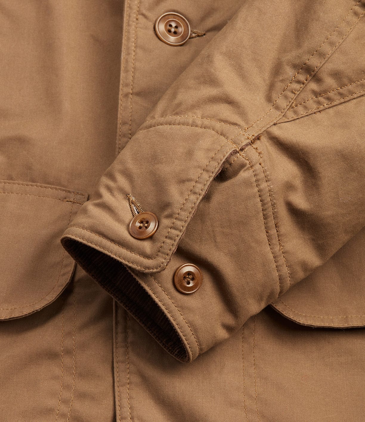 Close-up of a Best Made Co. Wool-lined Waxed Field Jacket Tan sleeve shows visible stitching, a buttoned cuff, and a flap front pocket. This all-weather jacket provides comfort and durability with its cotton-blend material and wool lining.
