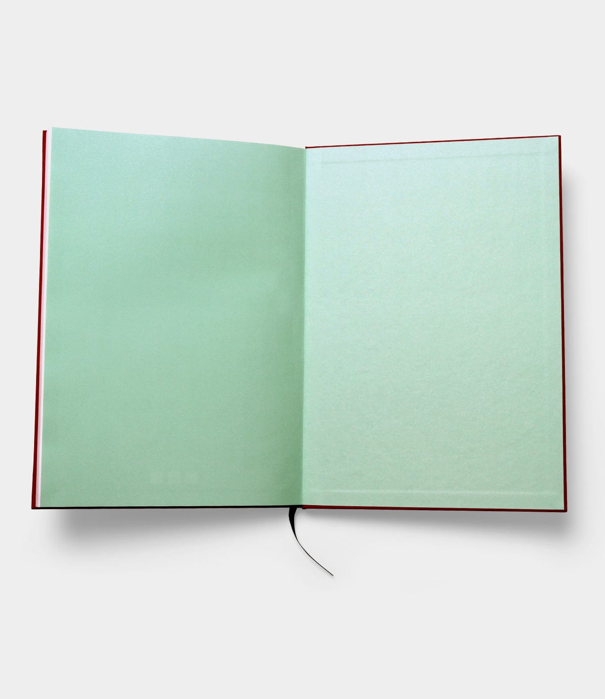 The S.B.T. Max Cloth-Bound Notebook by Best Made Co. features pale green blank pages and a black ribbon bookmark, elegantly complementing its open, cloth-bound hardcover design as it lies flat on a white surface.