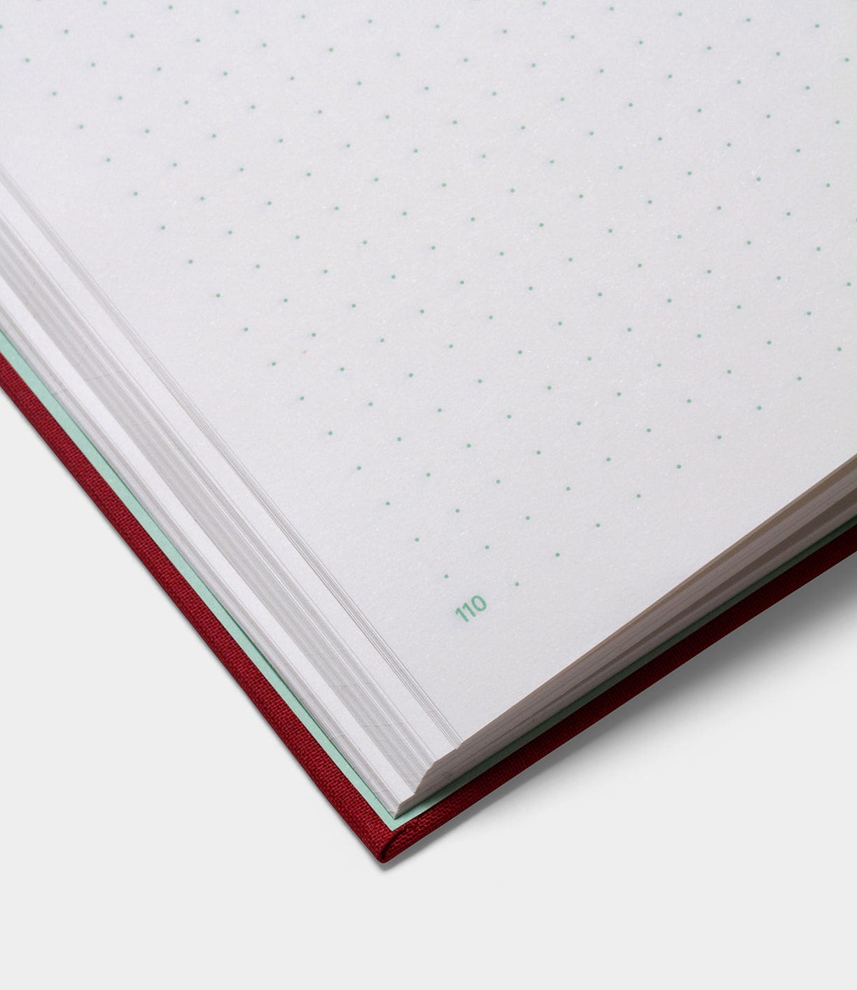 Close-up of the S.B.T. Max Cloth-Bound Notebook by Best Made Co., a red hardcover with white dotted grid pages; corner of page 110 is numbered in green.