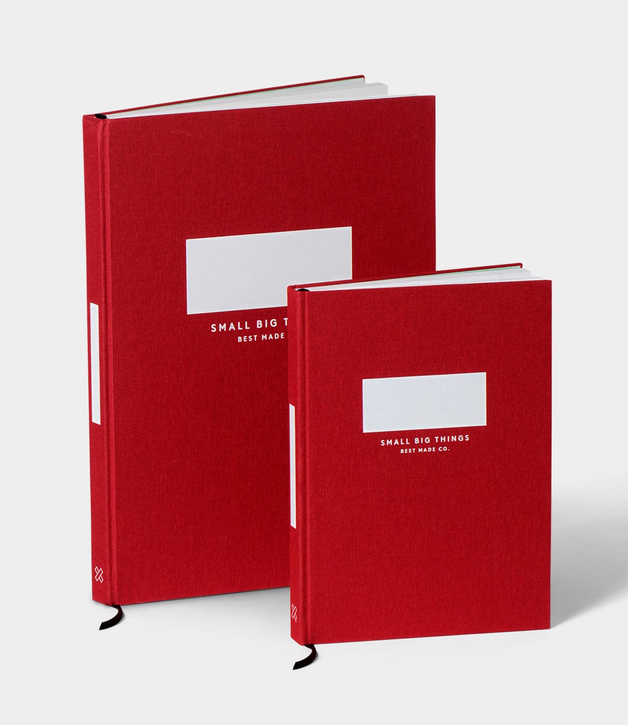 Two red S.B.T. Max Cloth-Bound Notebooks by Best Made Co. of different sizes stand upright, each hardcover with a white label and white text. The background is plain and light-colored.