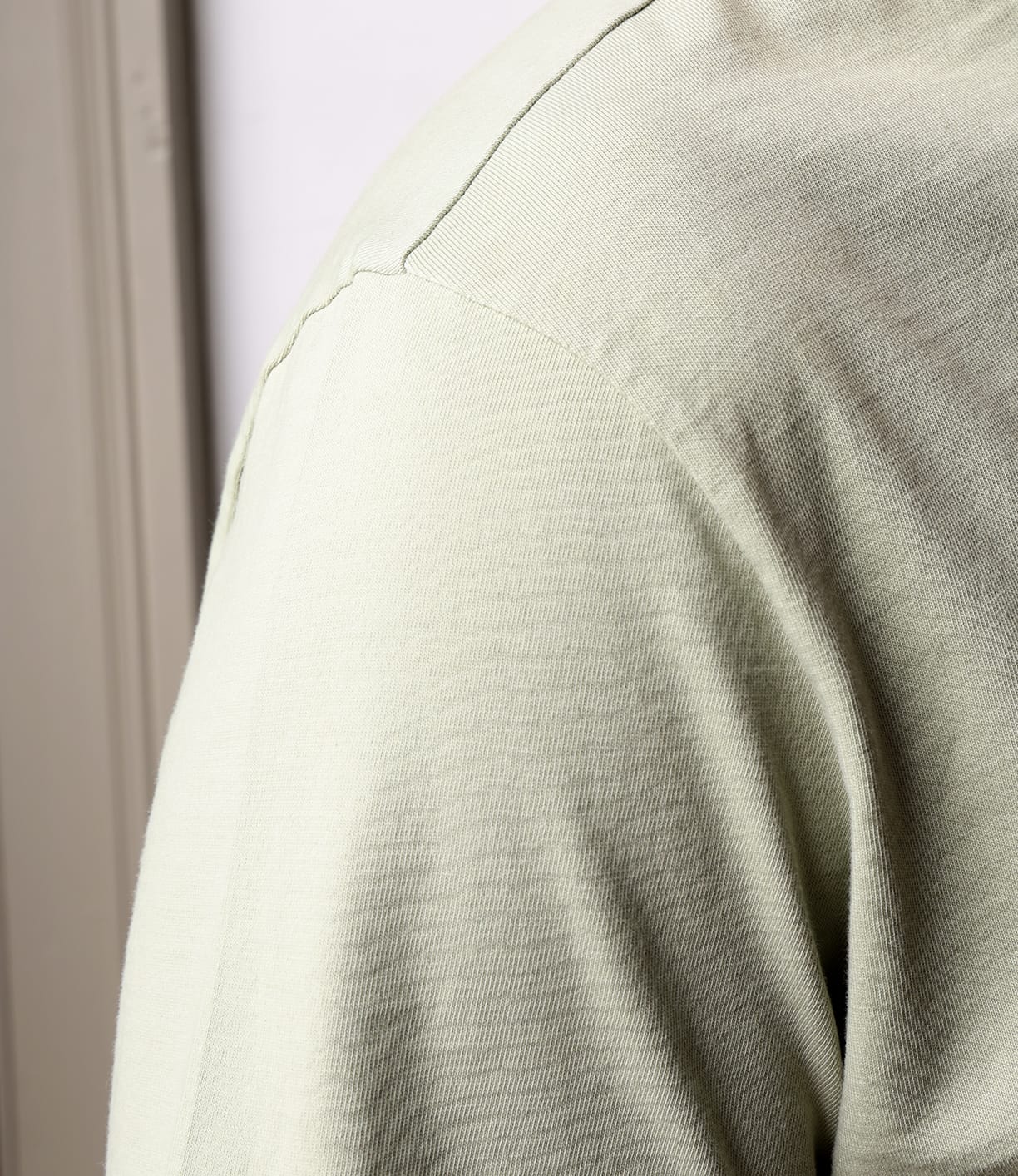 Close-up of a shoulder wearing the Best Made Co Standard Pocket T-Shirt Haze in light beige, highlighting ribbed texture and seam details. Crafted from soft Peruvian tangüis cotton against a subtly blurred neutral background.