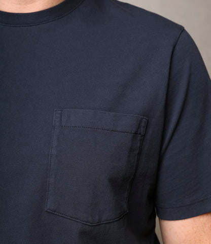 Close-up of a person wearing the Best Made Co. Standard Pocket T-Shirt Navy—garment-dyed, made from Peruvian tangüis cotton, featuring a left chest pocket. Only the upper torso and part of the arm are visible.