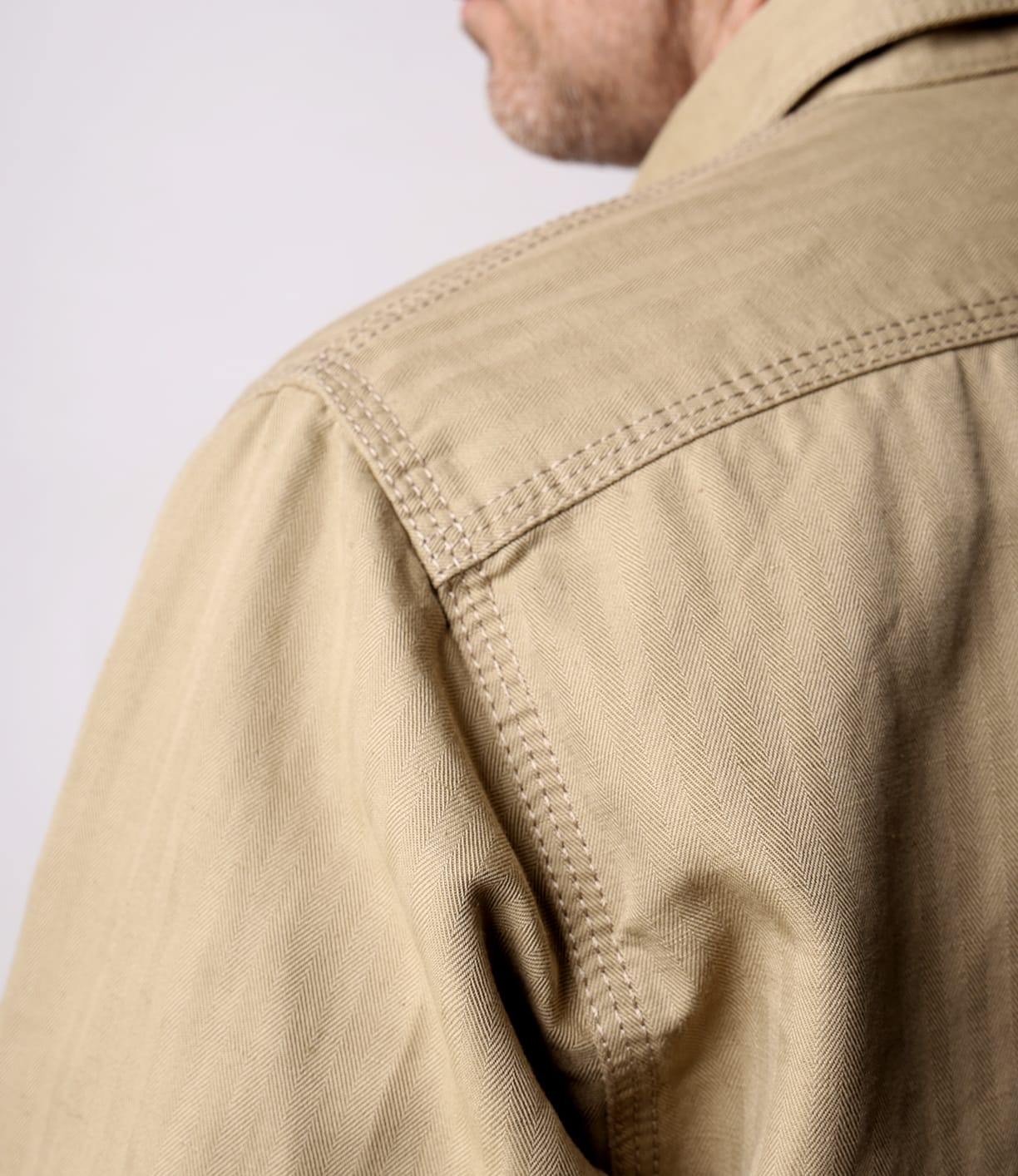 Close-up of a person wearing the Best Made Co. Cotton-Linen Workshirt Tan, highlighting detailed shoulder and upper back stitching. The collared shirt's texture is visible as the wearer’s face is partially turned from the camera.