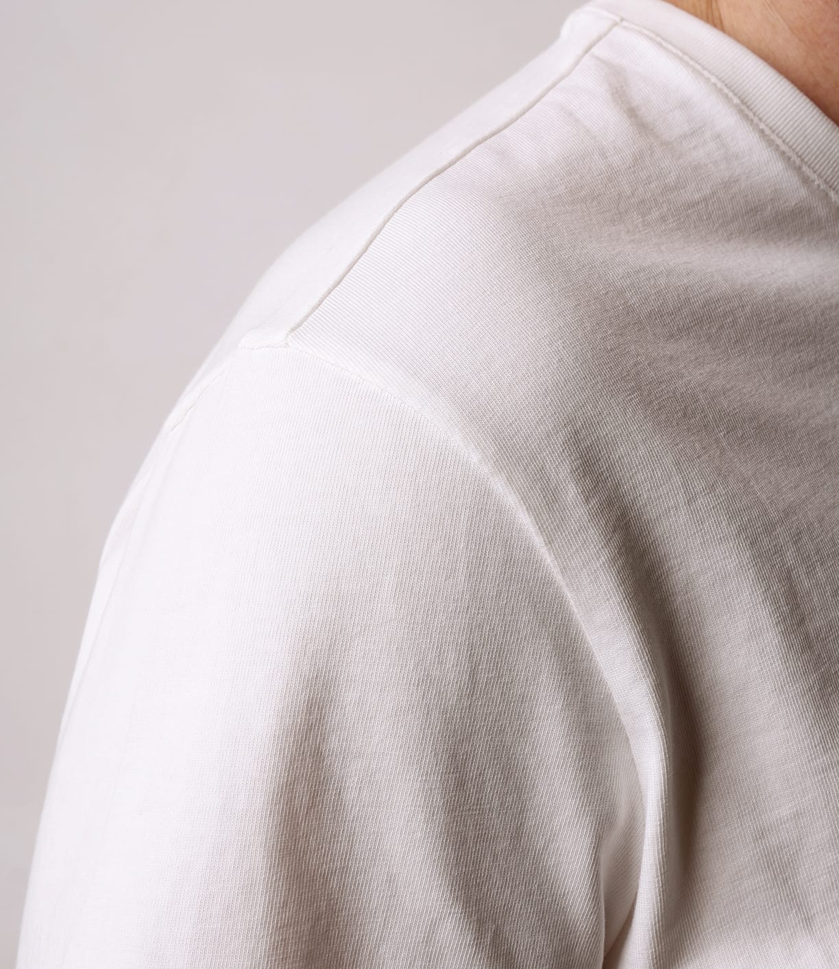 Close-up of a person wearing the Best Made Co Standard T-Shirt Undyed, made from durable white Peruvian tangüis cotton, showing only their shoulder and upper arm against a plain light background. The head and most of the body are out of frame.