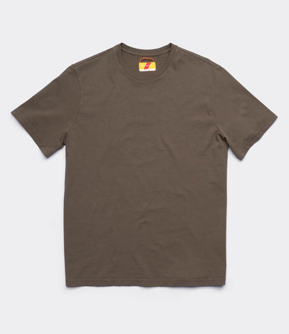 The Best Made Co. Standard T-Shirt Field Drab is a solid olive green, garment-dyed short-sleeve crew neck made from soft Peruvian tangüis cotton, shown flat on white with a small colorful design on the inner neck tag.