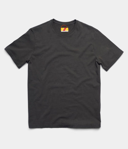 The Best Made Co. Standard T-Shirt in Faded Black, featuring short sleeves and a round neckline, is laid flat on a light gray background with a small, colorful tag visible inside the collar.