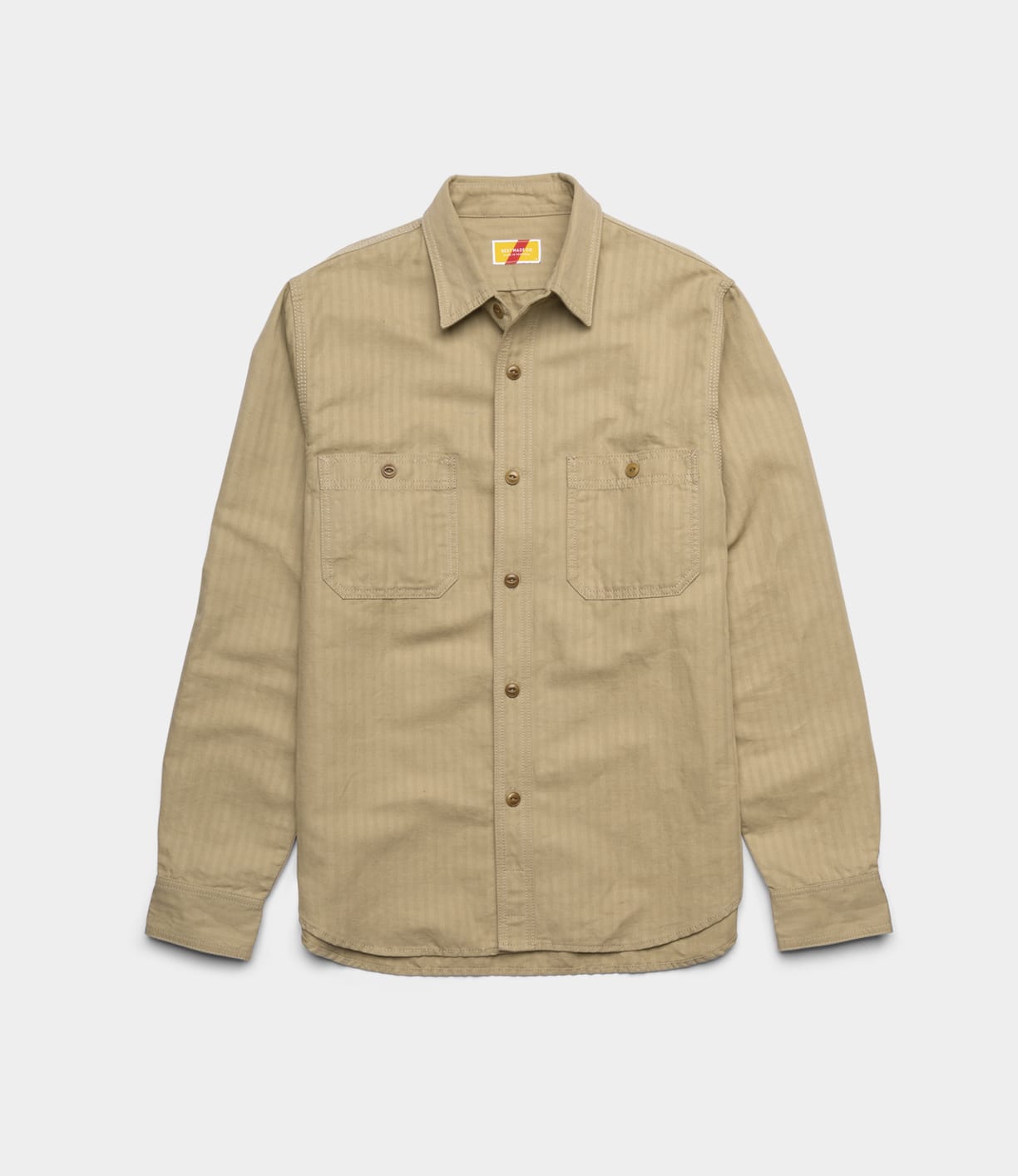 The Best Made Co. Cotton-Linen Workshirt Tan, with long sleeves, button-up front, chest pockets, and a collar, is laid flat on a white background—a refined workwear staple.