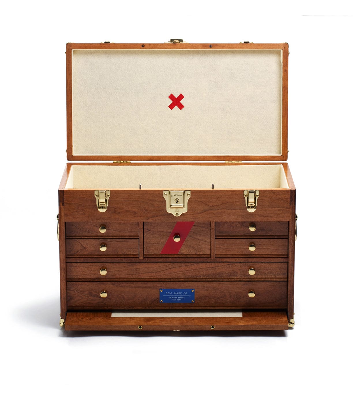 The Best Made Co. 41D Gerstner Chest 2026, crafted from American cherry with brass hardware, features an open lid showing a cream interior, several drawers, a red X on the lid, and a blue nameplate on the lower front drawer.