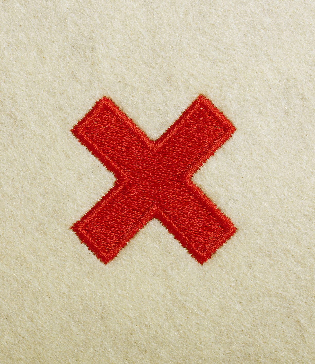 A red embroidered X symbol stands out on light beige fabric, echoing the classic detail often seen on the 41D Gerstner Chest 2026 by Best Made Co.