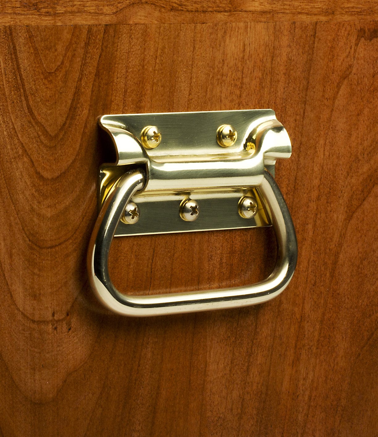A shiny brass handle with a rectangular base, fastened by four screws, is mounted on the Best Made Co. 41D Gerstner Chest 2026, which features smooth American cherry wood with a rich reddish-brown finish.