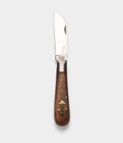 The Best Made Co. Anchor Knife features a polished metal sheepsfoot blade, a dark wooden handle with brass anchor inlay and rivets, displayed on a plain light gray background.