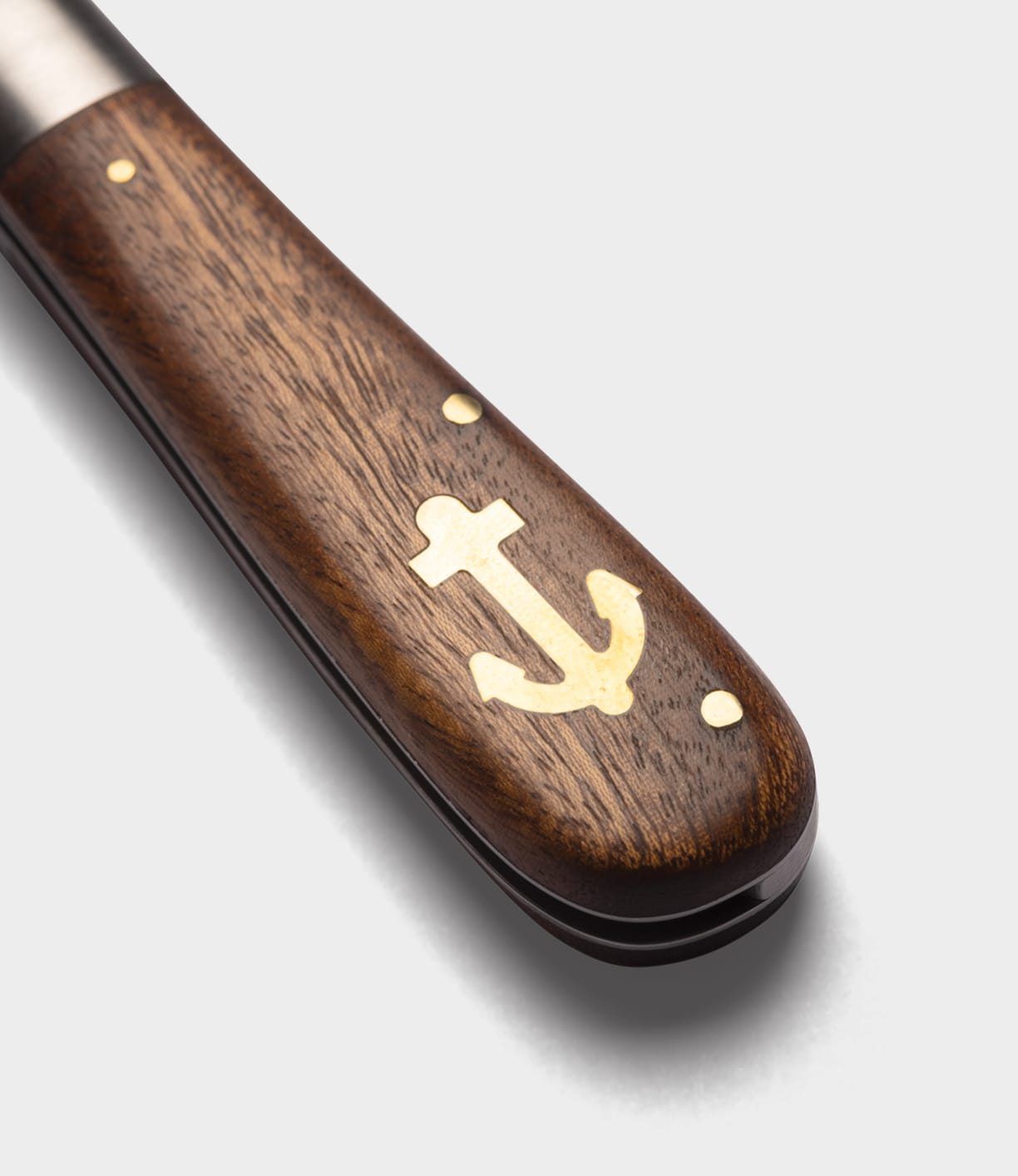 Close-up of the Best Made Co. Anchor Knife featuring a wooden handle with a brass anchor inlay and two brass rivets, set against a plain light gray background.