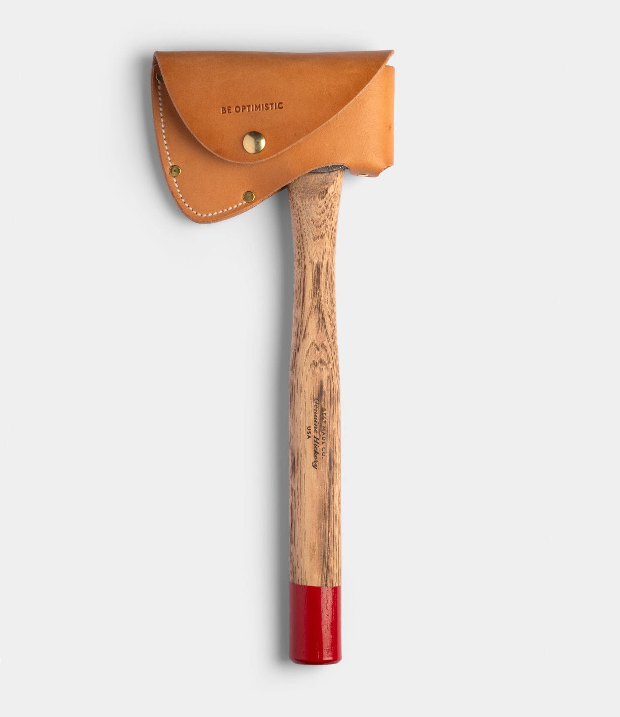 The Spark (Straight-Hold Edition) by Best Made Co. is a high-carbon steel axe with an Appalachian hickory handle, red-painted end, and a tan leather sheath stamped "BE OPTIMISTIC" with a brass button, set against a plain light gray background.