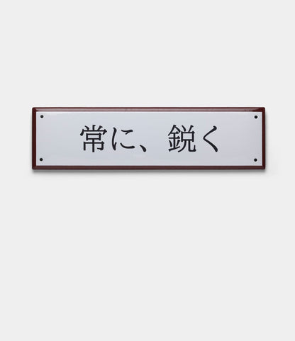 The Best Made Co. “Stay Sharp” Enamel Steel Sign (Kanji Edition) features a handcrafted rectangular white enamel design with black 常に、鋭く text, red-brown border, and is inspired by the precision of Japanese blades.