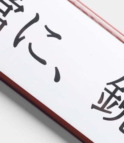 The “Stay Sharp” Enamel Steel Sign (Kanji Edition) by Best Made Co. is a white rectangular sign with black Japanese kanji and a dark brown border, shown angled and partly cropped on a light gray background.