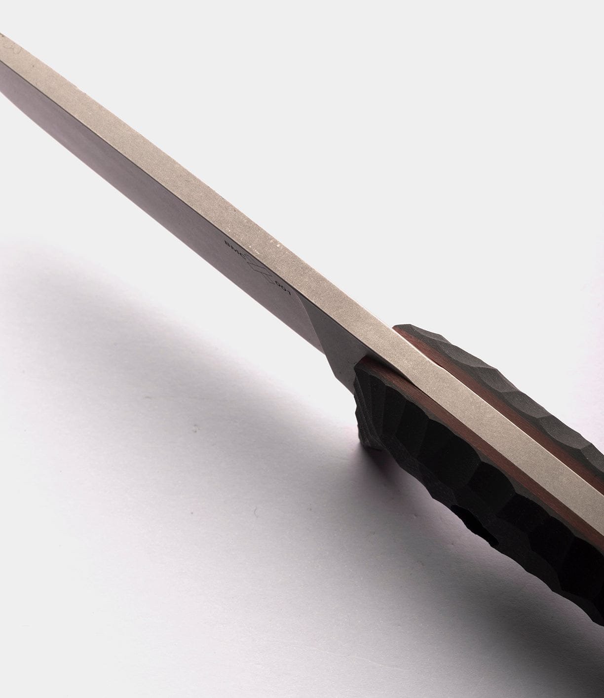 Close-up of the spine and handle of The NWBW Field Knife (BMC Edition) by Best Made Co, highlighting its textured grip and sharp American D2 tool steel blade edge against a light background.