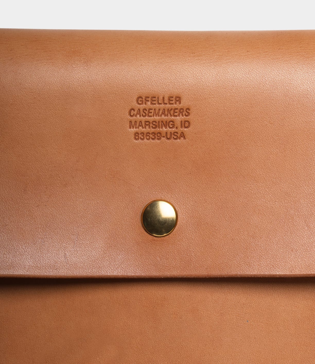Close-up of the tan Gfeller Case Small by Best Made Co. with a gold snap button and "GFELLER CASEMAKERS MARSING, ID 83639-USA" embossed above it on this hand-stitched leather case.