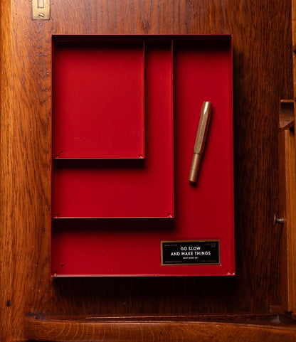 The Best Made Co. Spare Parts Trays (Set of 3), Go Slow Edition, in red with a gold pen and a "GO SLOW AND MAKE THINGS" label, are perfect for tool organization or as stackable trays on any wooden surface.