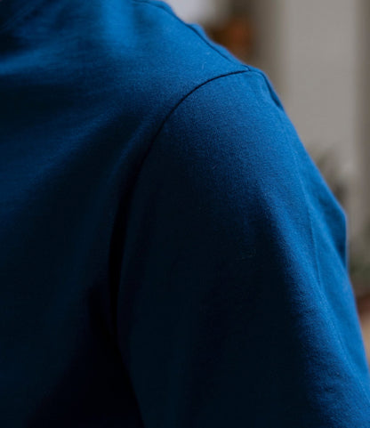 Close-up of a person wearing the Best Made Co. Standard T-Shirt in Signal Blue, focusing on the shoulder and upper arm. The softly blurred background highlights the rich blue color and premium quality of this Peruvian tangüis cotton tee.
