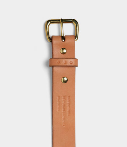 A Standard Belt by Best Made Co. in tan bridle leather, with a gold-colored buckle, two decorative rivets, and embossed text, made in the USA; shown vertically against a plain white background.
