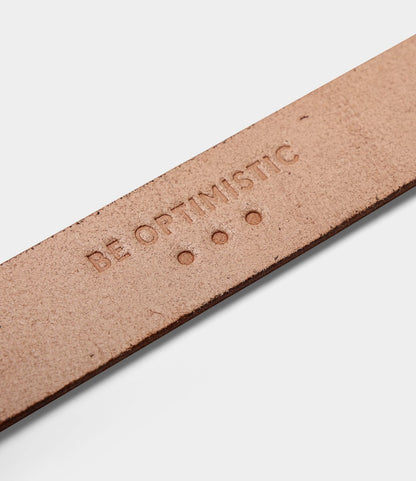 A close-up of a tan bridle leather strap from Best Made Co.'s Standard Belt, made in the USA, embossed with "BE OPTIMISTIC" and three small dots.