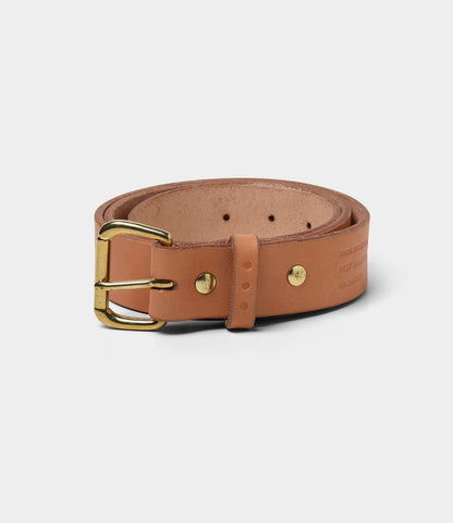 A rolled-up tan bridle leather Standard Belt by Best Made Co., featuring a gold-colored metal buckle, made in the USA, displayed on a light gray background.