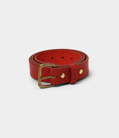 The Famous Red Belt by Best Made Co. is crafted from bridle leather in the USA, featuring a brass buckle and metal rivets, and is shown rolled up on a plain light gray background.