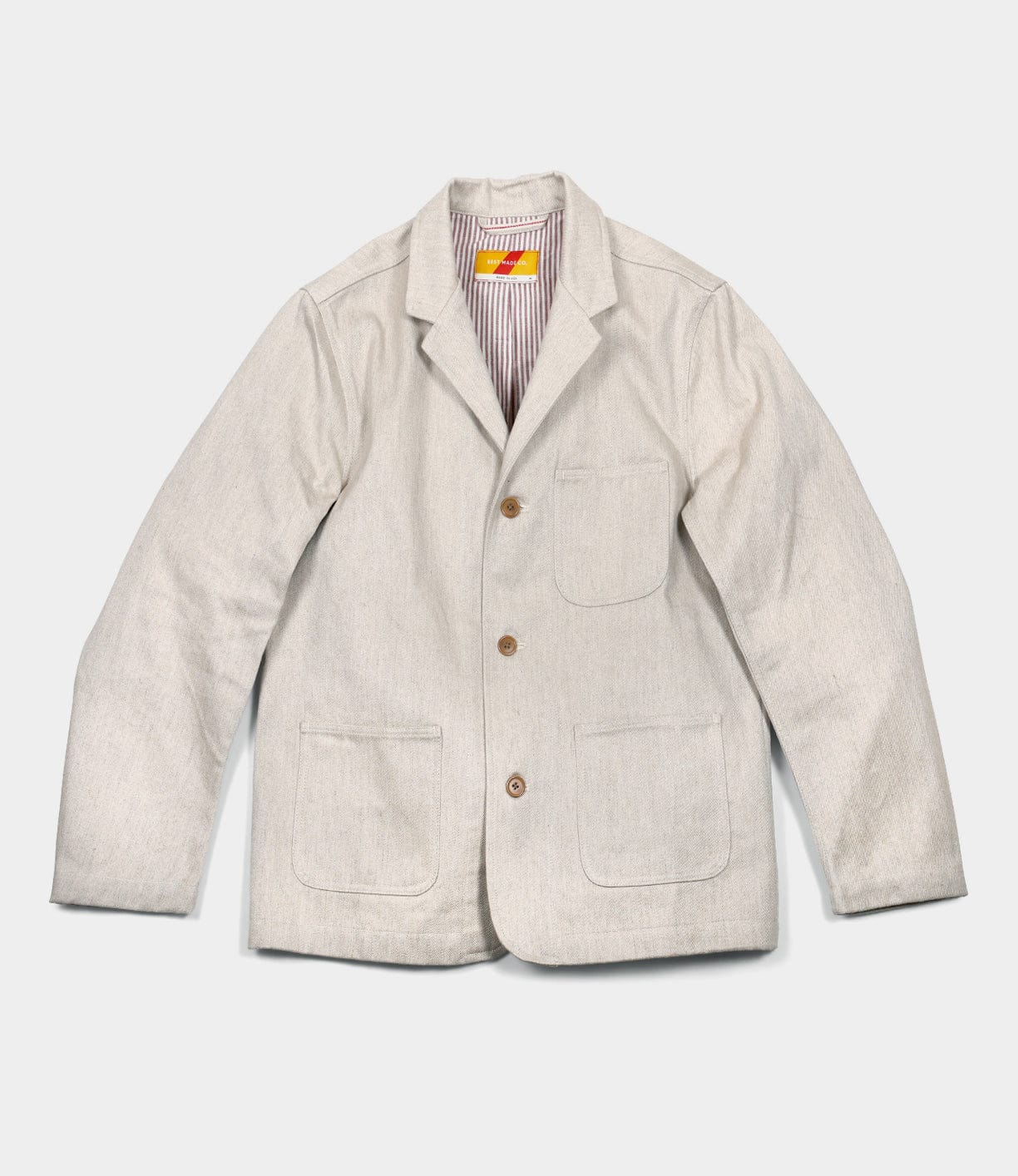 The Selvedge Beige Studio Jacket by Best Made Co features three front pockets, brown buttons, and a subtle striped lining—crafted in the USA. Displayed flat on a white background.